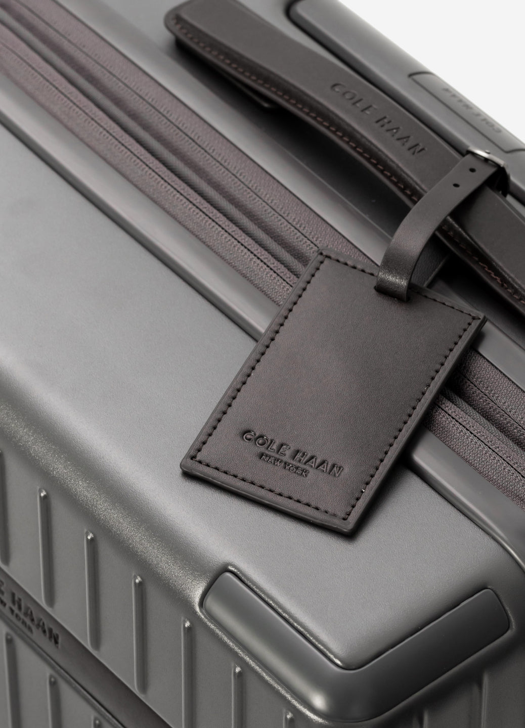 Gray suitcase with a matching leather luggage tag featuring the brand name.