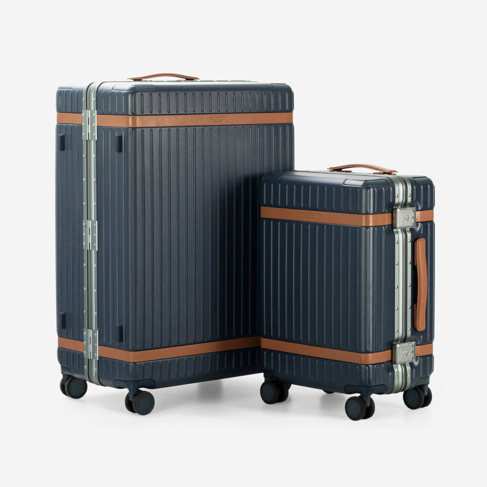 Two hard-shell spinner suitcases in dark navy blue with brown leather trim and silver metal hardware, shown on a clean light gray background.
