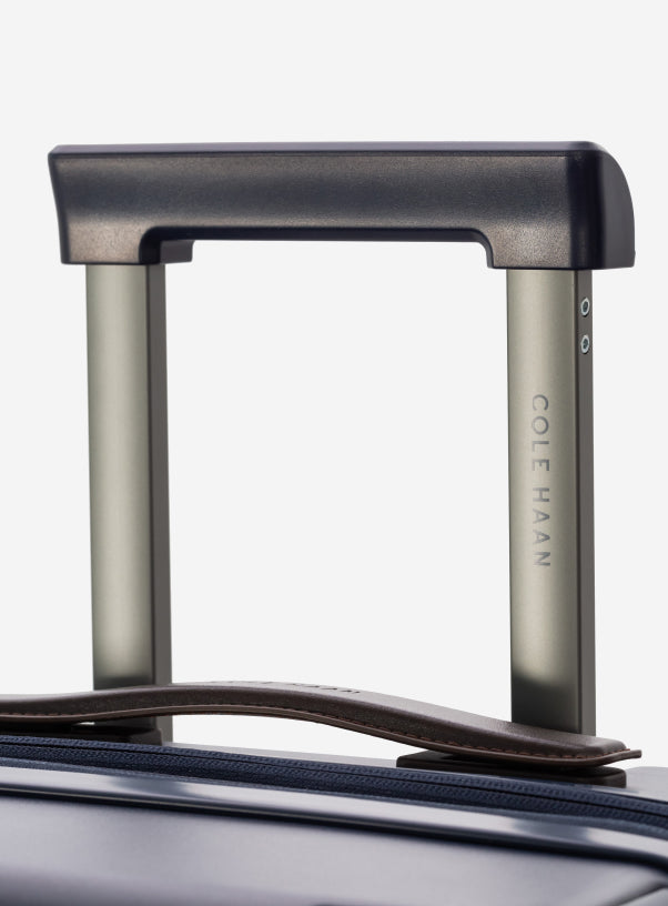 Close-up of a suitcase handle with 'Cole Haan' branding on a light gray background