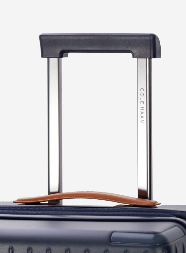 Close-up of a navy blue suitcase handle with 'Cole Haan' branding on a white background