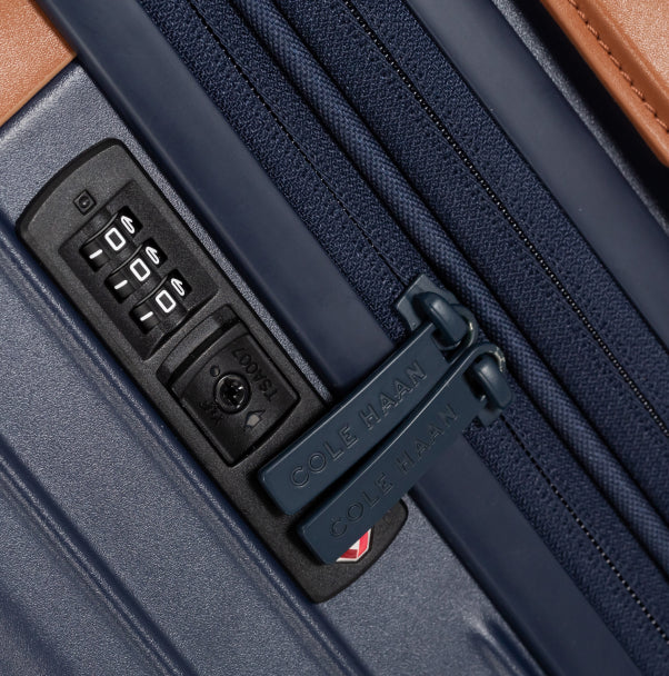 Close-up of a navy blue suitcase zipper with a combination lock and Cole Haan branding.