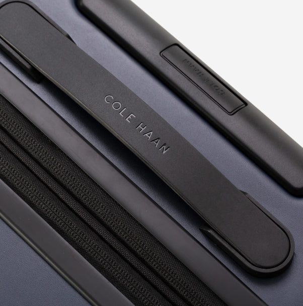 Close-up of a navy blue Cole Haan suitcase handle on a light gray background