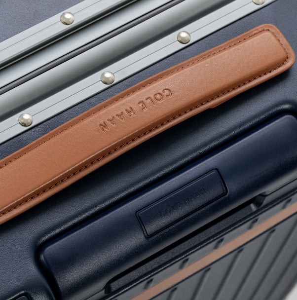 Close-up of a navy blue Cole Haan suitcase with a brown leather handle.