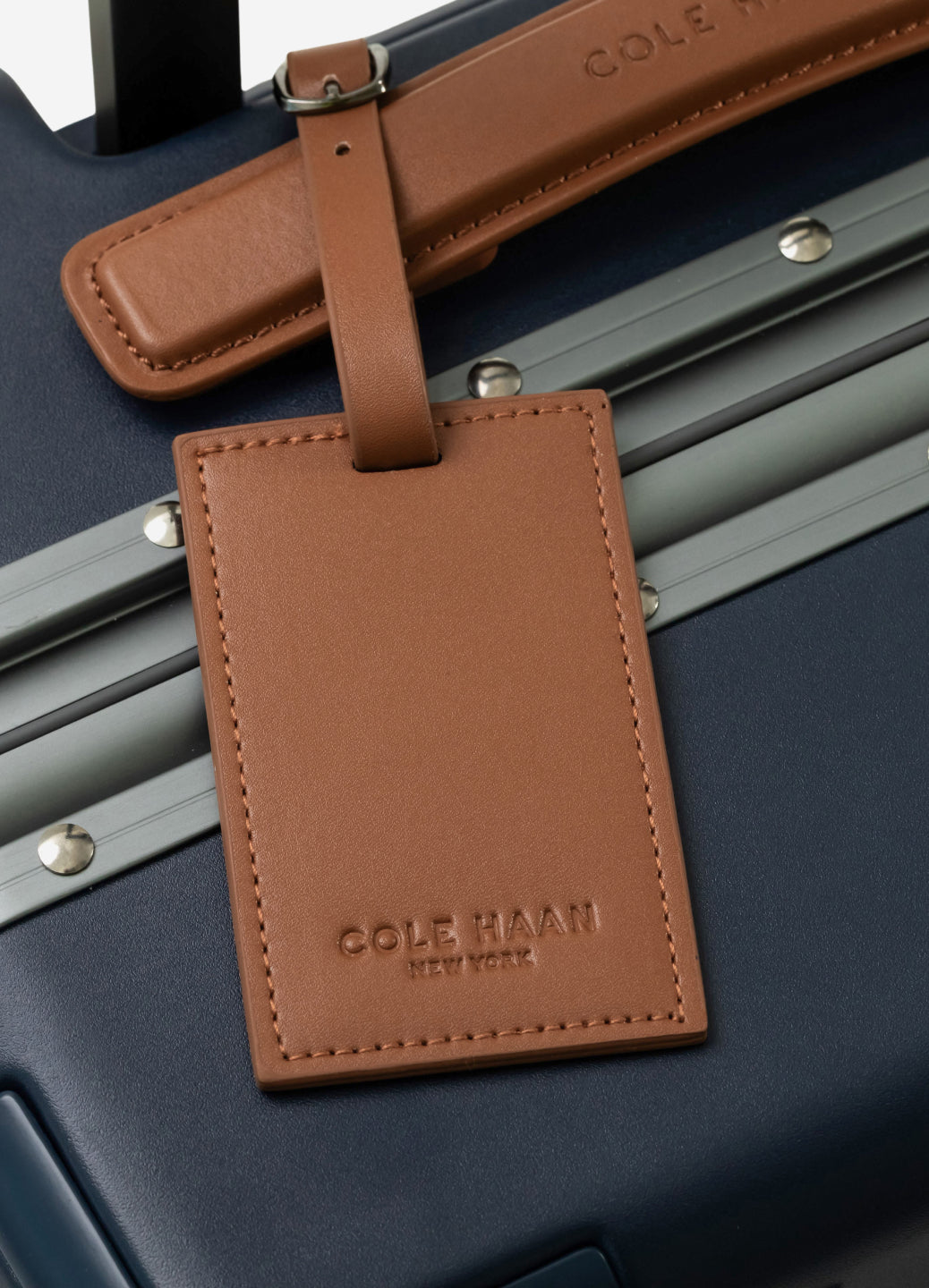 Brown leather luggage tag on a navy suitcase with 'Cole Haan' branding.