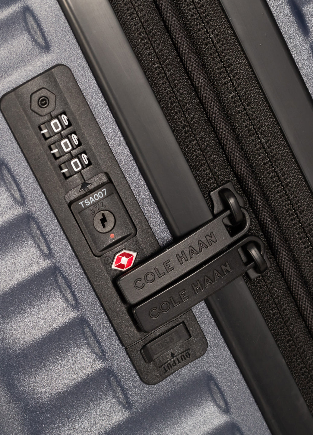 Close-up of a navy suitcase with a combination lock and Cole Haan branding.