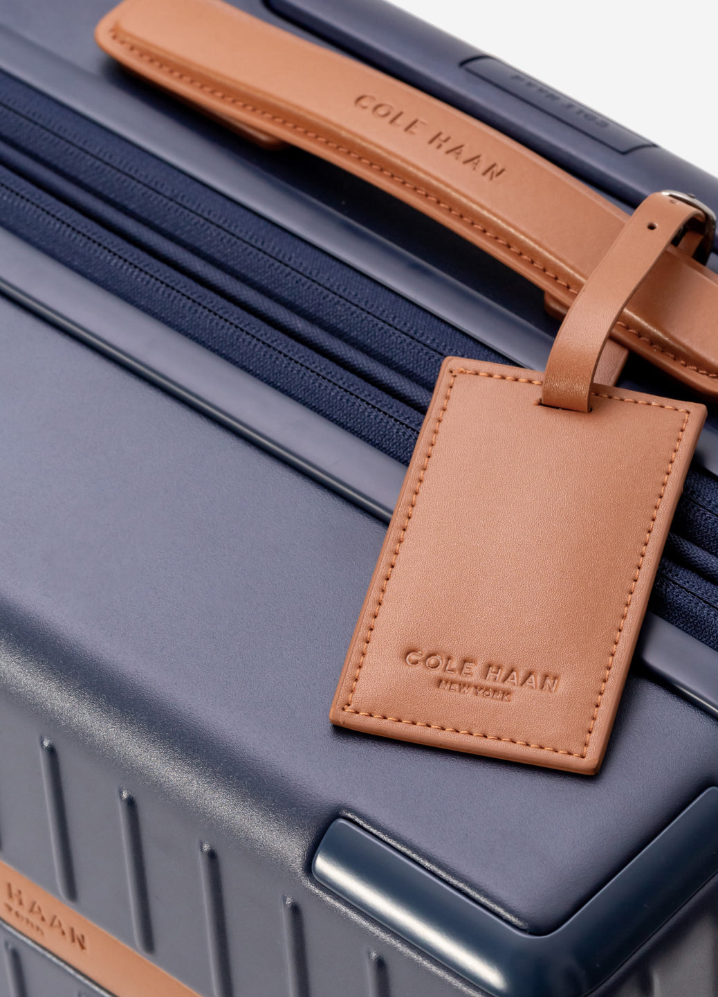 Navy suitcase with a brown leather luggage tag featuring 'cole haan' branding.