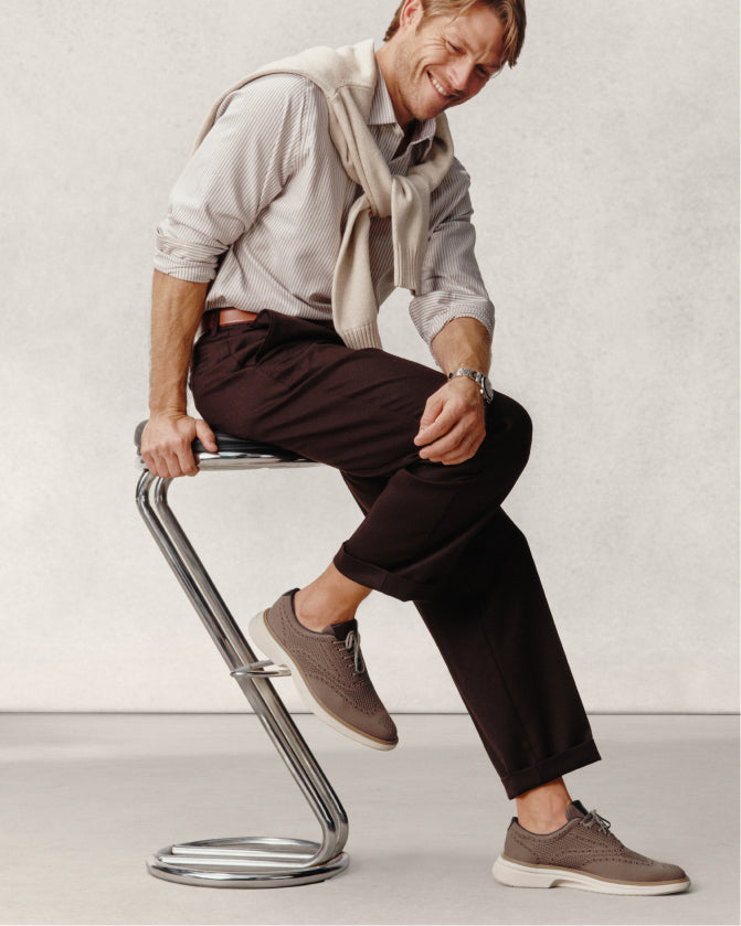 Man sitting on a modern metal stool against a plain background